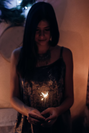 beautiful stylish woman holding  burning sparkler bengal light. glowing shining sparkler closeup in female hand in dark. merry christmas concept. happy new year eve celebrationの写真素材