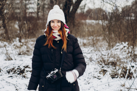 stylish hipster traveler girl with old photo camera exploring in snowy woods in winter. happy woman walking in cold forest. space for text. atmospheric moment. wanderlustの写真素材