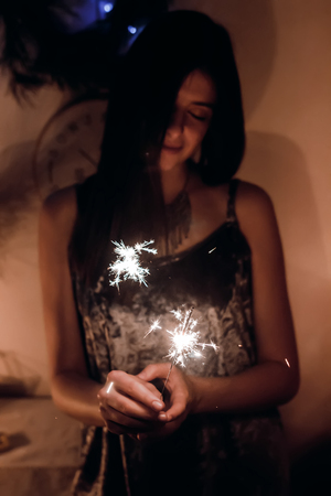 beautiful stylish woman holding  burning sparkler bengal light. glowing shining sparkler closeup in female hand in dark. merry christmas concept. happy new year eve celebrationの写真素材