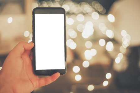 hand holding smart phone with empty screen on background of christmas lights in evening.の写真素材