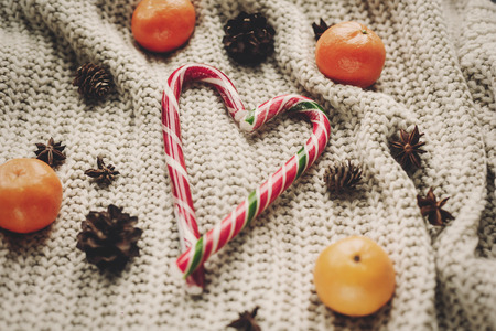 stylish peppermint candy cane in heart shape and pine cones and anise with tangerine on rustic knitted sweater background top view, space for text.  seasonal greetings.  merry christmas conceptの写真素材