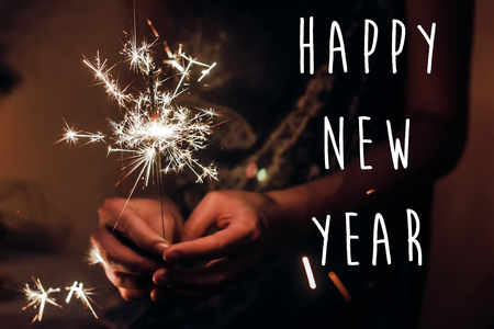 happy new year text sign, greeting card.happy new year and merry christmas concept. female hand holding a burning sparkler bengal light.  shining fire flame fireworksの写真素材