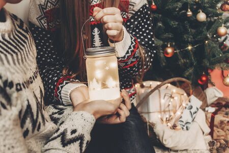 happy couple in stylish sweaters holding lantern light in festive room at christmas tree. happy holidays. atmospheric festive moments. merry christmas and happy new year conceptの写真素材