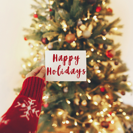 happy holidays text, seasons greetings, hand card on background of beautiful christmas tree lights. merry christmas and happy new year concept. seasonal greetingsの写真素材