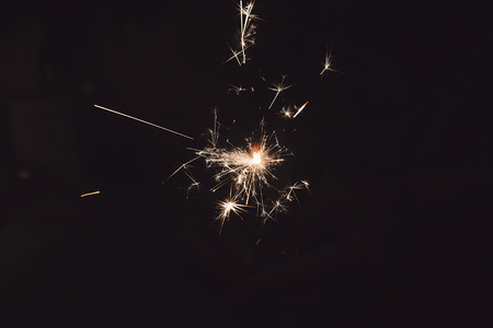 hand holding a burning sparkler firework bengal light. space for text. burning sparks closeup in female hand in dark. happy new year and merry christmas concept. happy holidays, tonedの写真素材
