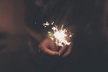 hand holding a burning sparkler firework bengal light. space for text. burning sparks closeup in female hand in dark. happy new year and merry christmas concept. happy holidaysの写真素材