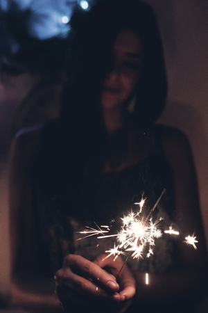 happy new year and merry christmas concept. happy stylish woman holding burning sparkler firework bengal light. space for text.  shining fire flame fireworks. happy holidays. tonedの写真素材