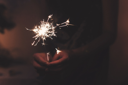 hand holding a burning sparkler firework bengal light. space for text. burning sparks closeup in female hand in dark. happy new year and merry christmas concept. happy holidaysの写真素材
