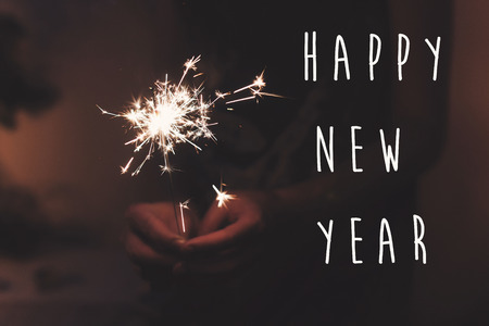 happy new year text sign, hand holding a burning sparkler firework bengal light. space for text. burning sparks closeup in female hand in dark. happy new year and merry christmas concept. happy holidaysの写真素材