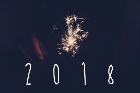 2018 happy new year text sign, hand holding a burning sparkler firework bengal light. space for...