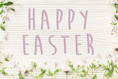 happy easter text sign, simple greeting card.  fresh daisy lilac flowers and green herbs frame on...