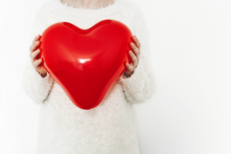 hands holding red heart balloon on white background with space for text.の写真素材