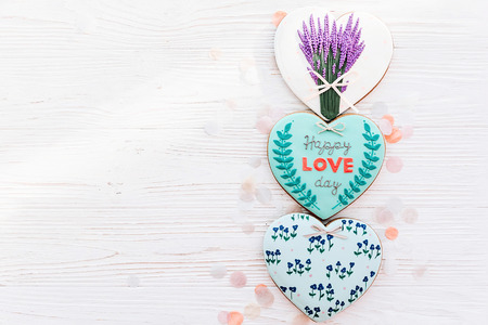 happy valentine's day greeting card. happy love day text on cookie heart and flowers on white rustic wooden background with confetti flat lay. space for text . mock-upの写真素材