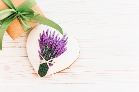 cookie heart with lavender flowers and craft gift box with green ribbon on white rustic wooden background with confetti flat lay. happy mother's day greeting card or women's. space for text .の写真素材