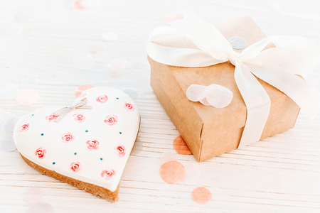 happy valentine's day greeting card. cookie hearts and craft gift box and confetti on white rustic wooden background. space for text. happy mother's day or women's. mock-upの写真素材