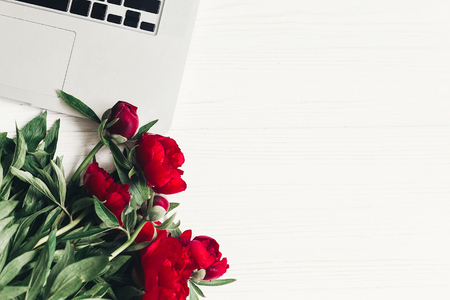 stylish laptop and beautiful red peonies on white wooden background flat lay.の写真素材