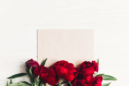 beautiful red peonies bouquet and craft paper card on white wooden rustic background, flat lay.の写真素材