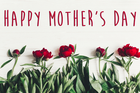 happy mother's day text sign on beautiful red peonies on white wooden rustic background, flat lay. modern greeting card. mothers day. stylish blooming flowers top viewの写真素材