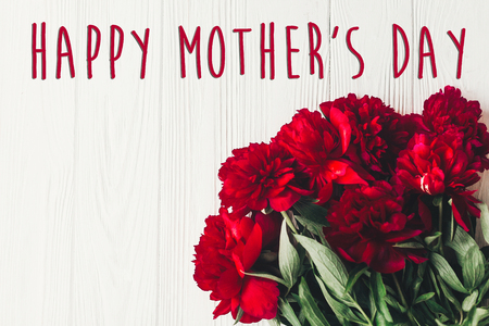 happy mother's day text sign on beautiful red peonies on white wooden rustic background, flat lay. modern greeting card. mothers day. stylish blooming flowers top viewの写真素材