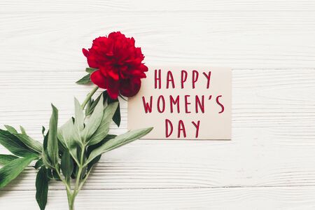 happy women's day text sign on craft card and beautiful red peonies on white wooden rustic background, flat lay. modern greeting card. womens dayの写真素材