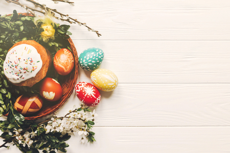 stylish easter eggs and easter bread cake and flowers on wooden background flat lay. modern eggs...