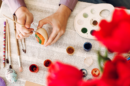 happy easter concept. hands holding and painting easter eggs on rustic table with paint and tulips. happy girl preparing for easter celebration and hunt.の写真素材