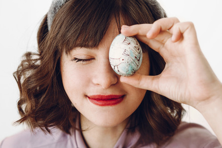 beautiful stylish girl in bunny ears holding easter egg at eyes and relaxing on white background with space for text. funny easter hunt concept. happy easter celebrationの写真素材