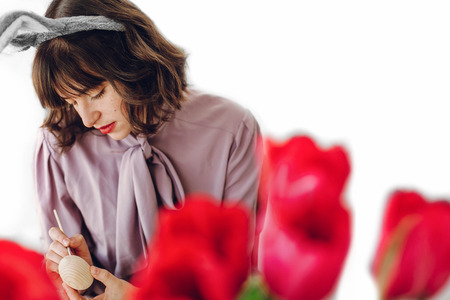 happy girl in bunny ears painting easter eggs on rustic table with paint and tulips at home. preparing for easter celebration and hunt. happy easter concept.  space for textの写真素材