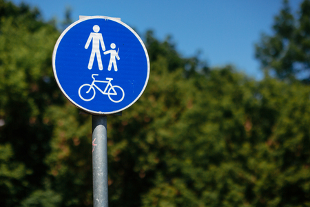 pedestrian bicycle zone sign in blue circle on background of green trees in park. city street sign concept. sign with person and child and bicycle in white and blue circle.の写真素材