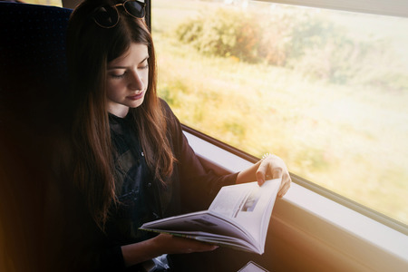 stylish hipster girl reading book at window light in train. travelling by train concept. beautiful...