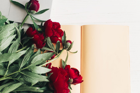 freelance concept. stylish laptop with note book and beautiful red peonies on white wooden background flat lay.の写真素材