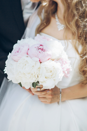 stylish bride with peony bouquet and groom in suit posing in sunny garden on wedding day. luxury wedding couple, happy newlyweds family. romantic momentsの写真素材