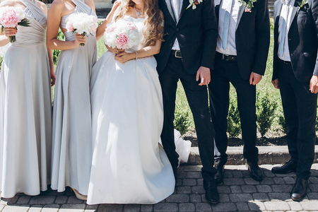 gorgeous bride with peony bouquet and stylish groom with bridesmaids and groomsmen posing in sunny garden for photo. luxury wedding couple having fun with friendsの写真素材