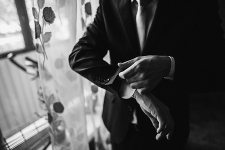 groom putting on suit. stylish man preparing for wedding ceremony in the room in morning. black and...