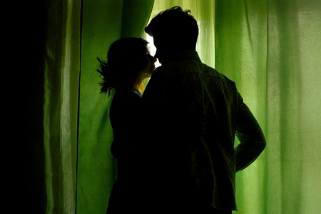 silhouette of couple standing at green curtains at window and huggingの写真素材
