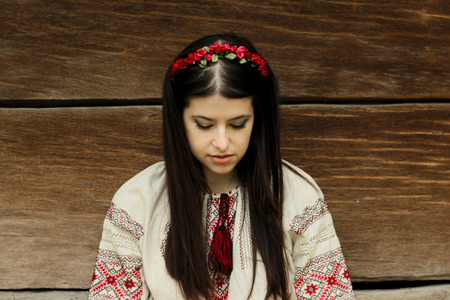 beautiful brunette woman in national ukrainian embroidery clothes on background of old native wooden...