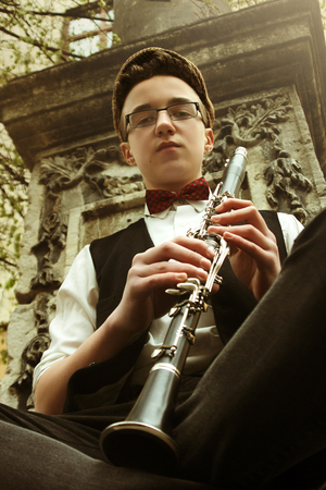 stylish hipster sitting man playing clarinet  on background of old city street, close up