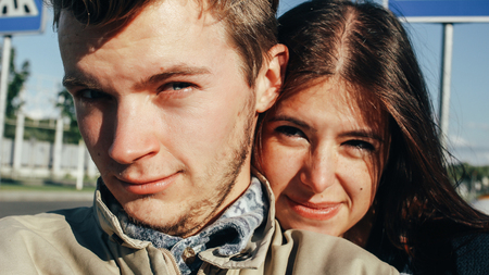 close up of happy emotional couple hugging and winking on background of urban city airport
