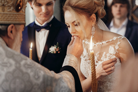 stylish bride and groom exchanging rings at matrimony in church. happy luxury wedding couple holding candles during ceremony . romantic moment.の写真素材