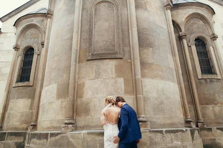 luxury wedding couple embracing at old building in in light. stylish bride and groom kissing her back  in city street. romantic sensual moment. man tenderly touching womanの写真素材