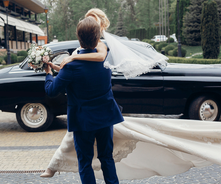 luxury wedding couple dancing at old car in light. stylish bride and groom hugging and embracing in city street. romantic sensual moment. woman looking at manの写真素材