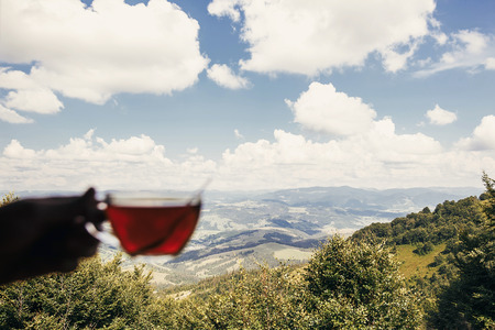 traveler holding glass of hot tea at window with view on mountains and sky. hipster man holding...