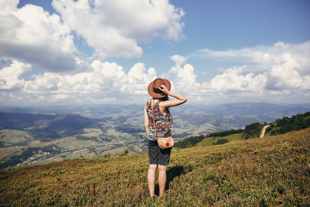 travel and wanderlust concept. stylish traveler girl in hat looking at sunny mountains and cloudssky. summer vacation. space for text. back view. amazing atmospheric momentの写真素材