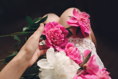 boho girl in white bohemia dress holding beautiful pink peonies on legs, top view. space for text. stylish hipster woman with flower in hand. moody morning. atmospheric sensual momentの写真素材