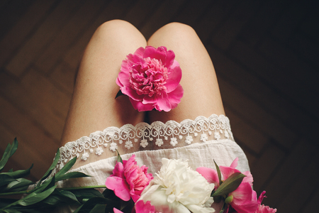 beautiful pink peonies on legs of boho girl in white bohemian dress, top view. space for text. stylish hipster woman sitting with flowers in moody morning. atmospheric sensual momentの写真素材