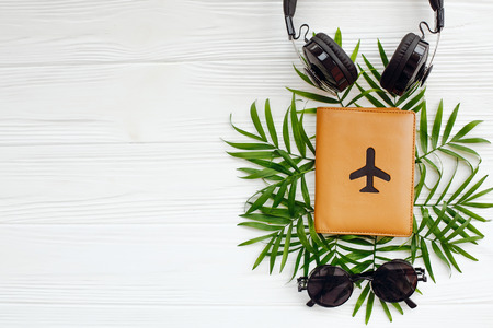 stylish summer flat lay. passport with plane, retro black sunglasses and headphones on green palm leaves on white wooden background. space for text. modern travel and vacation imageの写真素材