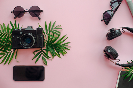 stylish black headphones with green palm leaves, photo camera, sunglasses and phone on trendy pink background, flat lay. modern hipster travel image. summer vacationの写真素材
