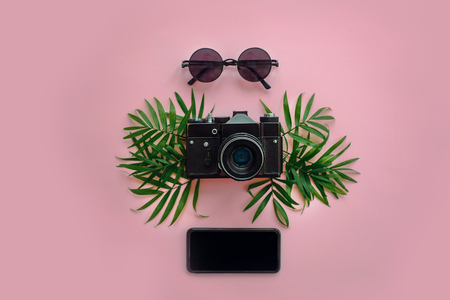 stylish black photo camera with green palm leaves, sunglasses and phone on trendy pink background, flat lay. modern hipster travel  image. summer vacation,space for textの写真素材
