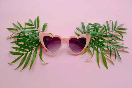 stylish pink sunglasses in heart shape and green palm leaves on pink background, flat lay. space for text. summer vacation concept. time to travel concept and relax. holidaysの写真素材