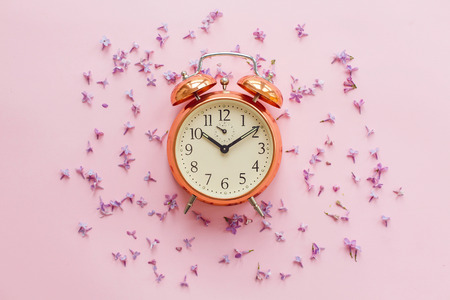 time concept. stylish vintage alarm clock on pink background with lilac flowers. creative flat lay with space for text.  modern fashion image. summer vacation. time to wake upの写真素材